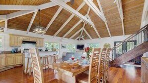 A spacious kitchen with wooden cabinets, a dining area with a wooden table and chairs, and a staircase leading to an upper level. - NEW Princeville Home for 12 with Mountain and Waterfall Views (Princeville)