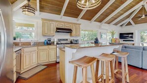 A spacious kitchen with wooden beams, a large island with stools, and a grey sofa in the living area. - NEW Princeville Home for 12 with Mountain and Waterfall Views (Princeville)