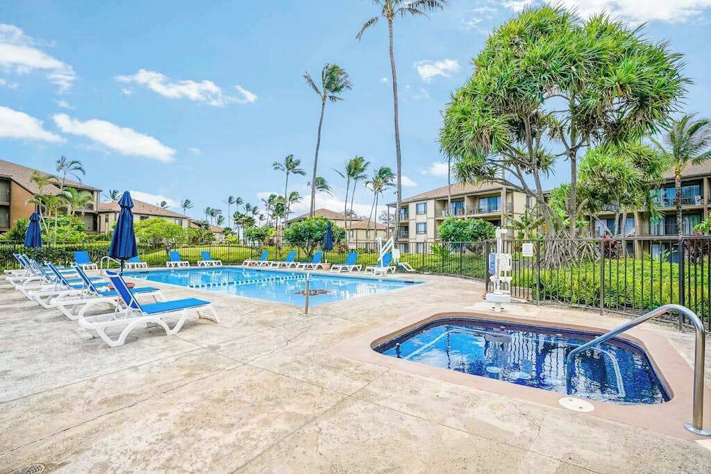 A hotel pool area with lounge chairs, a hot tub, and palm trees.