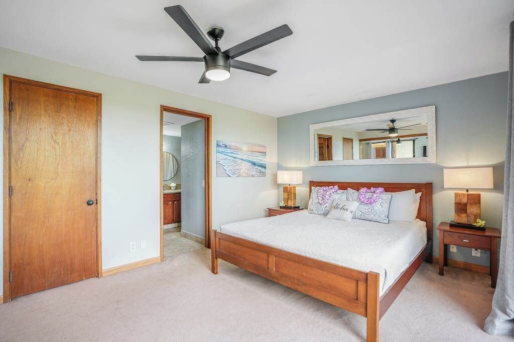 A bedroom with a wooden bed, a ceiling fan, a nightstand with a lamp, a mirror, and a door.
