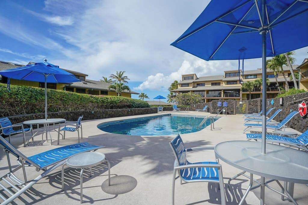 A pool area with lounge chairs, umbrellas, and a clear sky.