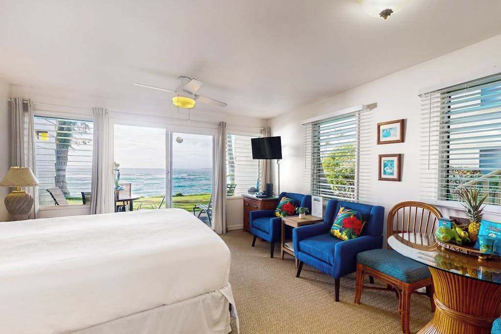 A hotel room with a bed, a desk, two chairs, a television, and a view of the ocean.