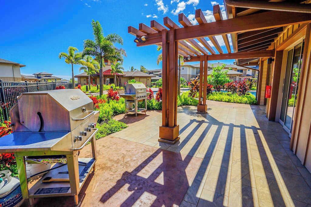 An outdoor patio with a grill, wooden pergola, and lush landscaping.