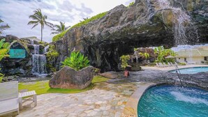 Ein Poolbereich mit Wasserfall, Palmen und einer Bank.