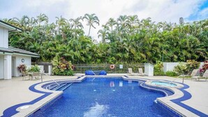 Ein Pool mit gewölbter Kante, umgeben von Palmen und einem eingezäunten Bereich mit Liegestühlen.