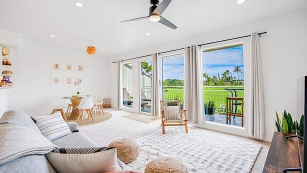 Ein modernes Wohnzimmer mit Sofa, Couchtisch und TV-Möbel. Es gibt einen Essbereich mit Tisch und Stühlen sowie einen Balkon mit Blick auf Grünflächen.