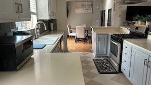 A modern kitchen with a built-in oven, a stove, and a sink. There is a dining area with a table and chairs.