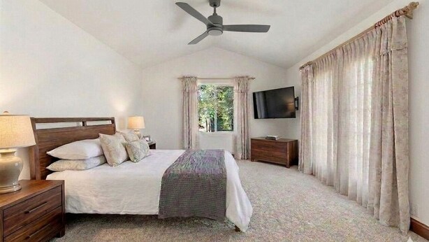 A bedroom with a bed, nightstands, a ceiling fan, a TV, and curtains.