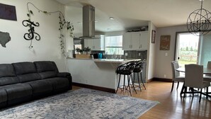 A living room with a sofa, a patterned rug, a kitchen with white cabinets, and a dining area with chairs.