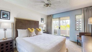 A hotel room with a bed, ceiling fan, two bedside lamps, a nightstand, a chair, and a view of the outdoors. - New Fall Special Kapaa 1BR with 3 Pools, 2 Hot Tubs and Beach Path (Kapaa)