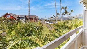 A balcony with a view of a parking lot, palm trees, and a building with a red facade. - New Fall Special Kapaa 1BR with 3 Pools, 2 Hot Tubs and Beach Path (Kapaa)