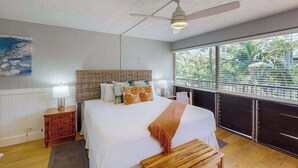 Ein Schlafzimmer mit Bett, Nachttisch, Deckenventilator und Fenster mit Blick auf Grünflächen.