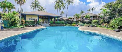 A swimming pool with lounge chairs, palm trees, and a covered area.