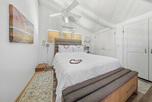 Ein Schlafzimmer mit einem Bett, einer Bank, einem Deckenventilator, einem Fenster mit Jalousien und einer Tür.