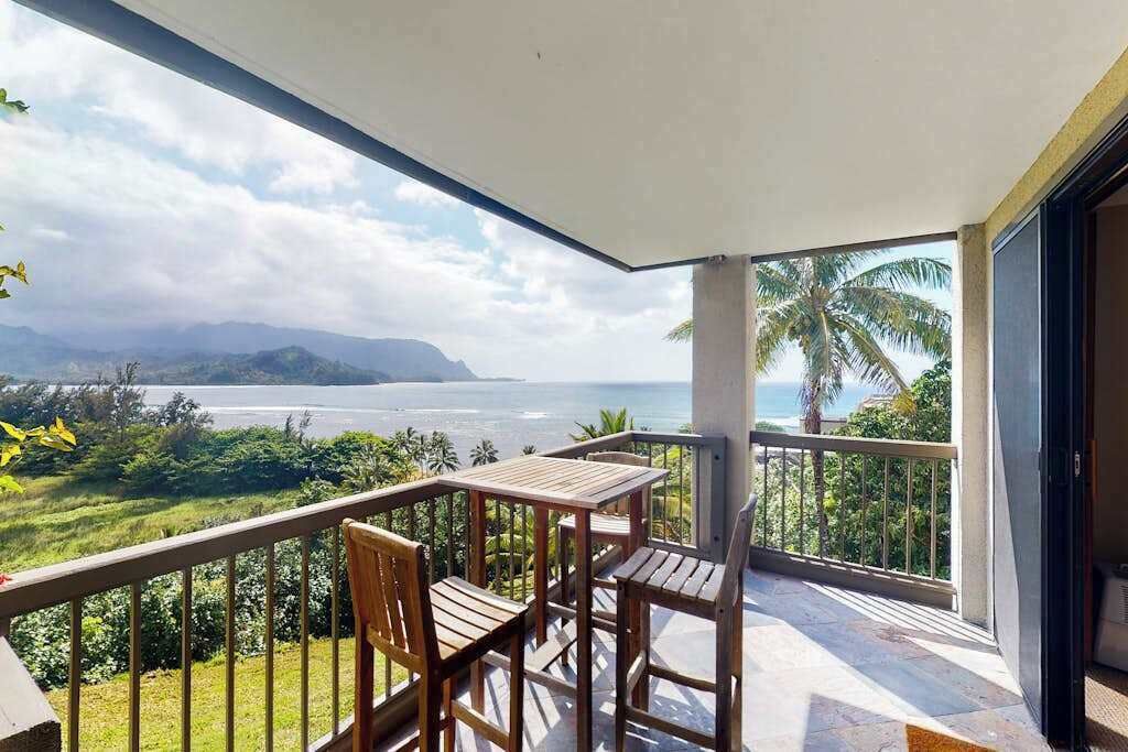 Un balcon avec une table et des chaises, une vue sur la mer et un palmier.