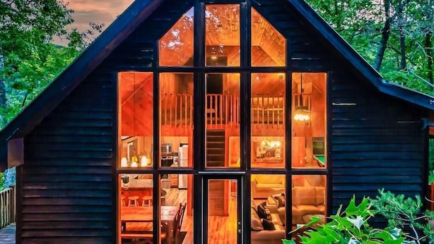 Una cabaña con un amplio ventanal, interior de madera y una terraza.