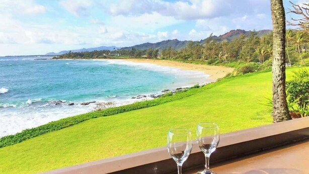 A view of a beach with two empty glasses on a balcony railing. - *New* Oceanfront Sunrise Retreat on Kauai's Coconut Coast (Kapaa)