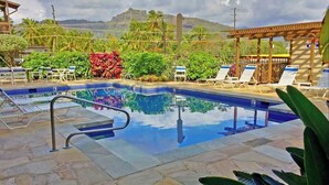 A swimming pool with lounge chairs and a pergola, surrounded by tropical plants and a mountainous backdrop. - *New* Oceanfront Sunrise Retreat on Kauai's Coconut Coast (Kapaa)