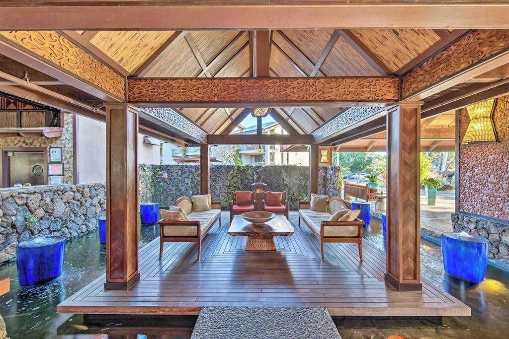 A covered outdoor seating area with a wooden deck, stone walls, and a water feature.