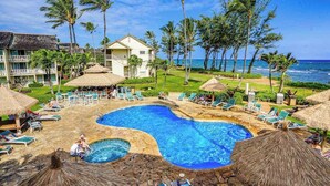 Un resort con piscina, sillas de descanso, palmeras y vista al océano.