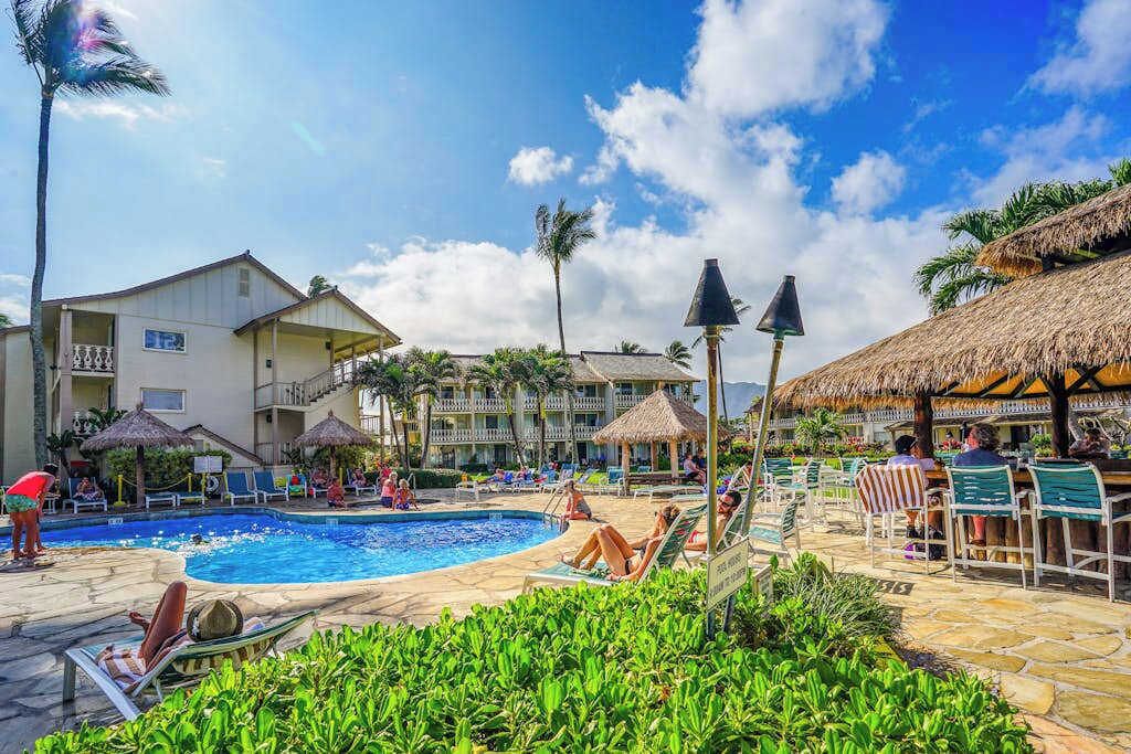 Ein Poolbereich eines Resorts mit Liegestühlen, Sonnenschirmen und einem Gebäude mit Balkonen.