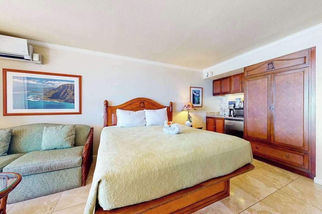 A hotel room with a bed, a sofa, a kitchen area, and a framed picture on the wall.