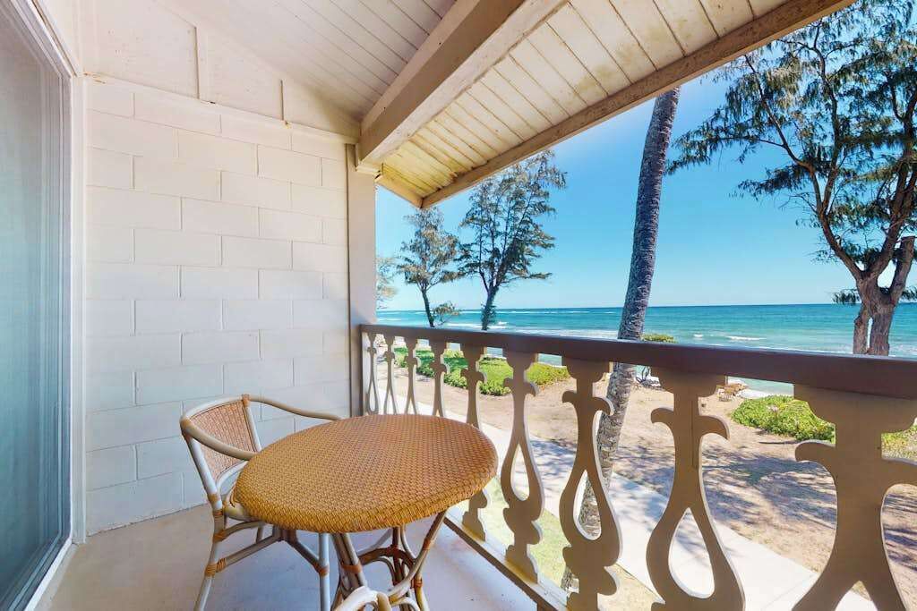 A balcony with a view of the ocean, a wicker chair, and a white brick wall.