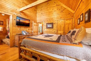 A wooden cabin interior with a bed, a desk with a computer, and a TV mounted on the wall. - Lazy Bear Lodge (Sevierville)