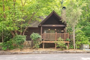 A cabin with a wooden deck, surrounded by trees. - Lazy Bear Lodge (Sevierville)