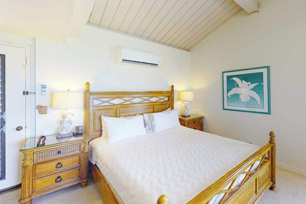 Une chambre à coucher avec un lit en bois, des tables de chevet, un climatiseur fixé au mur et un tableau encadré.