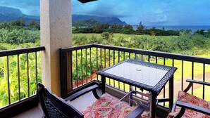 Un balcón con una mesa y sillas, con vistas a un paisaje exuberante y el océano.