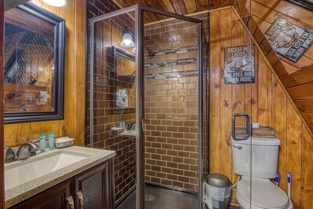 A bathroom with a wooden interior, a glass shower enclosure, a toilet, and a sink with toiletries.