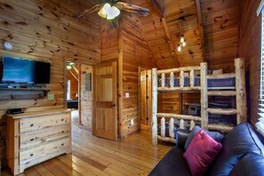 A log cabin interior with a wooden floor, a sofa with cushions, a television, and a bunk bed. - Kick Back Shack (Sevierville)