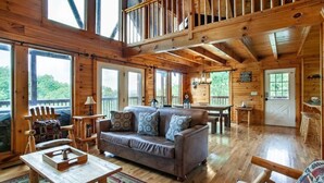 A cabin interior with a wooden floor, a sofa, a dining table, and a balcony with a railing. - Kick Back Shack (Sevierville)