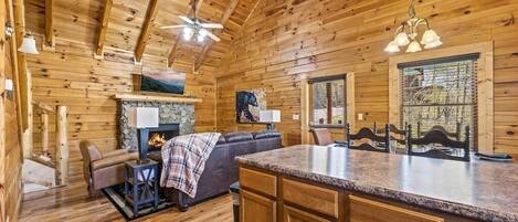 Ein Holzblockhaus mit Kamin aus Stein, einer Couch, einem Essbereich und einem Deckenventilator.