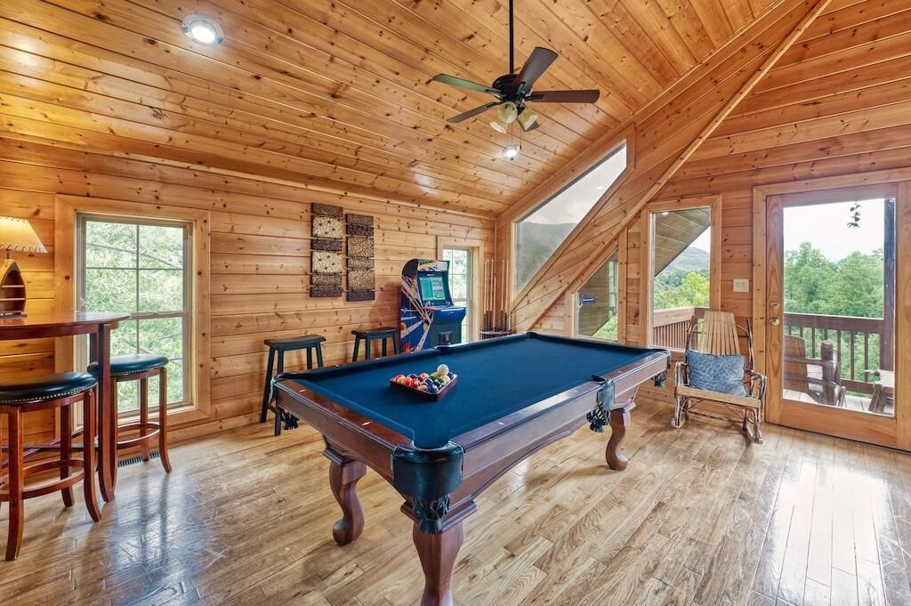 A wooden interior with a pool table, bar stools, and a ceiling fan.