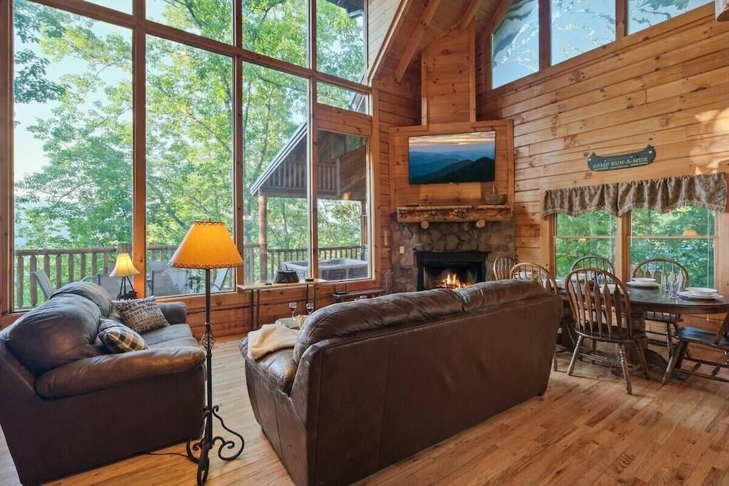A cabin interior with a fireplace, wooden walls, a sofa, a dining table, and a TV.