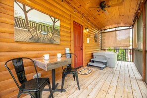 En stuga byggd av trä med en veranda, ett bubbelbad och ett bord med stolar.
