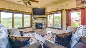 A living room with a fireplace, leather sofas, a flat-screen TV, and large windows. - Misty Mountain Stop (Sevierville)