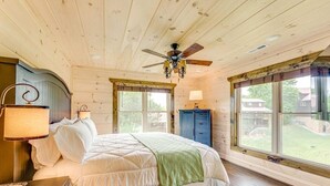 A bedroom with a bed, a ceiling fan, a lamp, a dresser, and large windows. - Misty Mountain Stop (Sevierville)