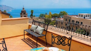 Eine Terrasse mit Frühstückstisch, einer Bank und Blick aufs Meer.