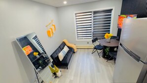 Un espacio habitable compacto con sofá, una mesa de comedor con sillas, un refrigerador y una ventana con persianas.