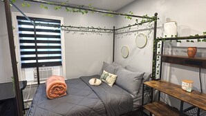 Un dormitorio con una cama, una mesita de noche, una ventana con persianas y un estante en la pared con adornos.