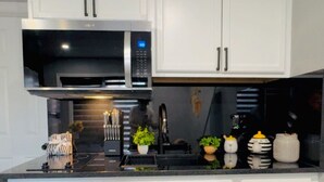 Una cocina moderna con armarios blancos, microondas integrado y encimera negra.