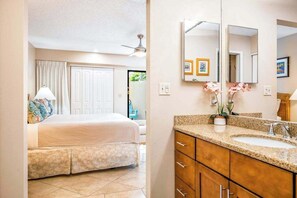 A hotel room with a bed, a bathroom with a sink and mirror, and a ceiling fan. - NEW Fall Special Ground-Floor Kihei Garden Condo Near Kamaole III (Kihei)