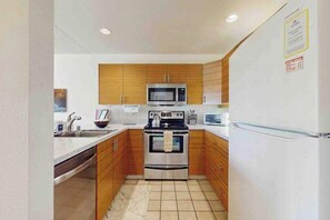 A compact kitchen with wooden cabinets, a stainless steel oven, a microwave, and a refrigerator. - Relaxing Kihei Condo with Garden View and Resort Pool Near Beach (Kihei)