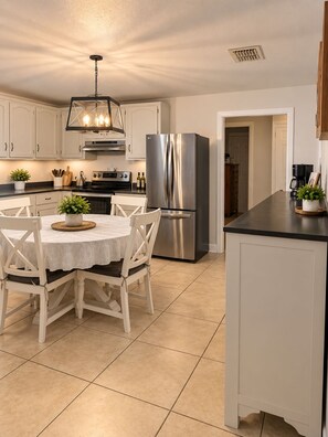 A modern kitchen with white cabinetry, stainless steel appliances, and a dining area with a round table and chairs. - Charming 3-bedroom house in Brownsville with cool AC breeze (Brownsville)