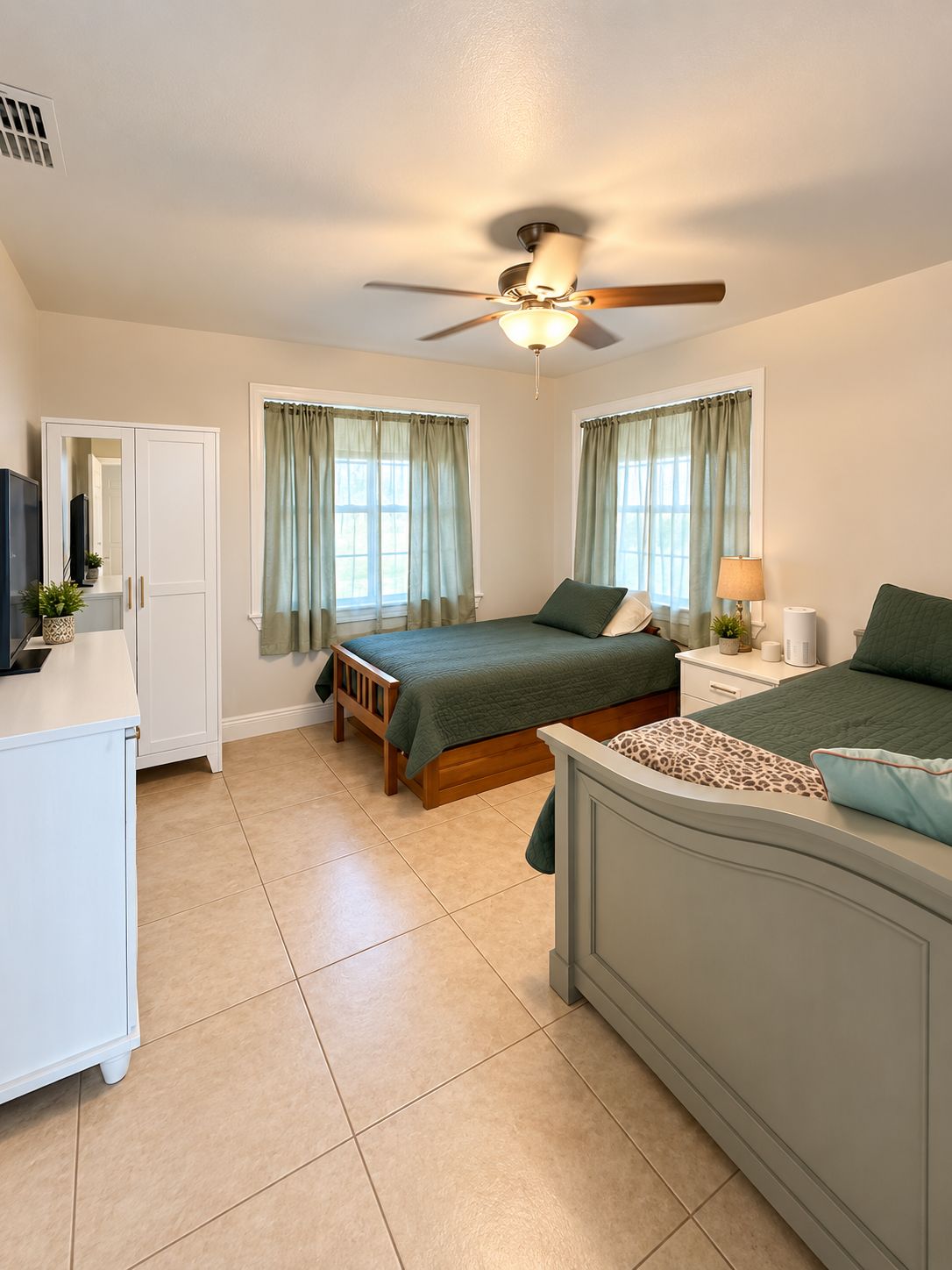 A bedroom with a bed, a nightstand, a desk, a ceiling fan, and a window with curtains.