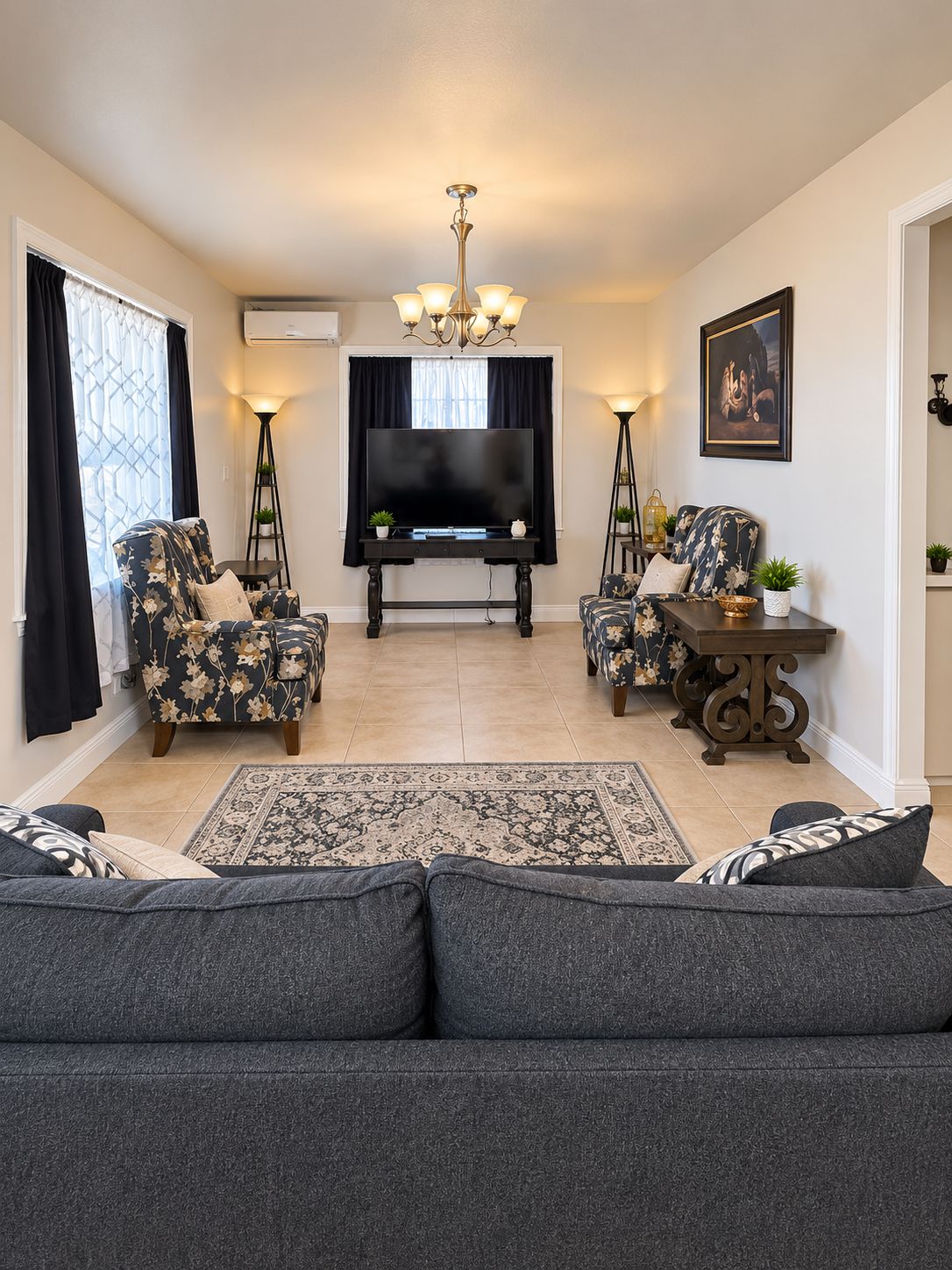 A living room with a sofa, two armchairs, a TV, a chandelier, and a rug.