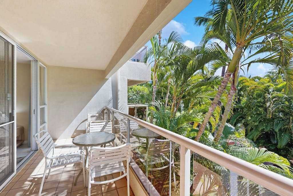 A balcony with a table and chairs, surrounded by tropical plants.